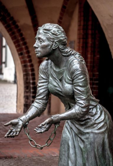 Bronzestatue einer Frau mit ergreifendem Ausdruck und Ketten an den Handgelenken.