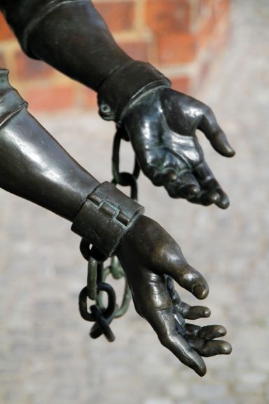 Skulptur von Händen mit Handschellen, die eine symbolische Gefangenschaft darstellen.